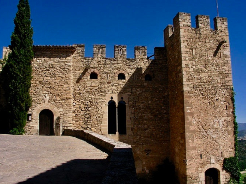 Castell de Montsonís, façade of the castle, main gateway, on the left a huge cypress tree. On the right, two arched windows and its great keep.
