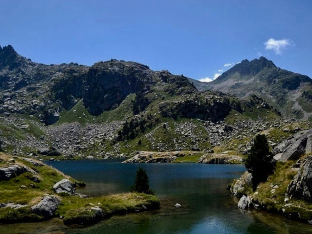 Llac major de Colomer, large mountains that reach the lake, with a blue summer sky.
