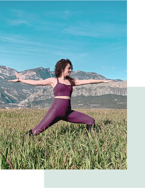 Chica practicando yoga en medio de un campo de trigo aún verde. Al fondo montañas con un cielo azul