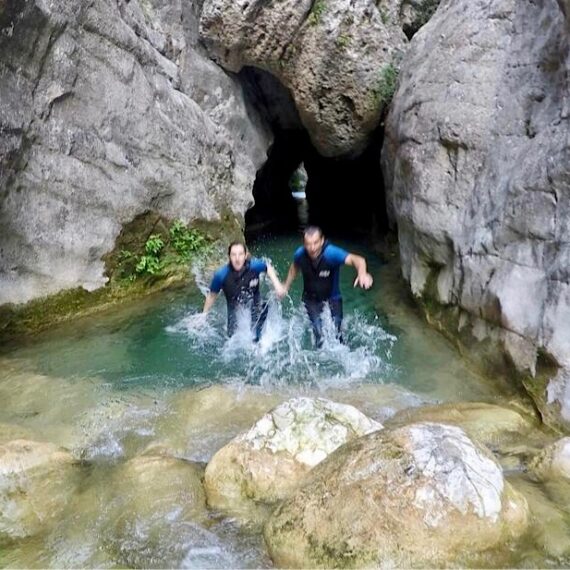 Couple smiling, dressed in wetsuits, coming out of the tunnel where the river Rialb flows down.