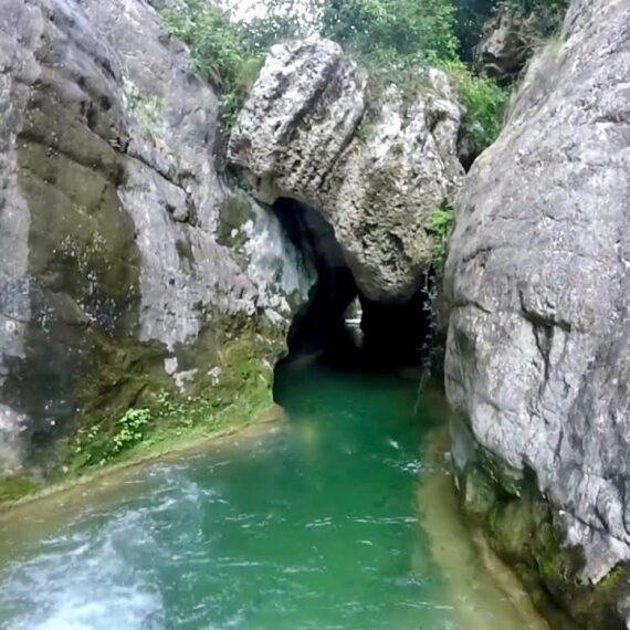 View of the river Rialb emerging from a greyish rock tunnel.