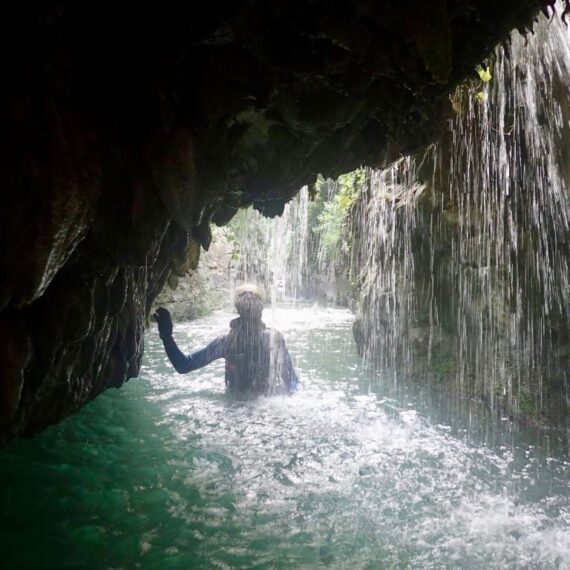 Persona en medio del río Rialb, ruta Forat de Buli, agua ahasta la cintura y el debajo de una cascada suave.