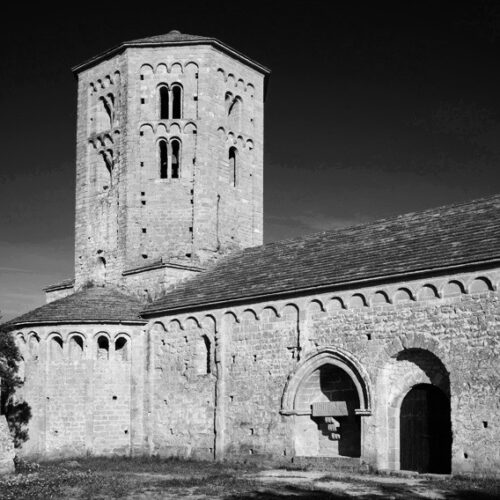 Vista de la porta de l'entrada nord de la col·legiata de Sant Pere de Ponts. Al costat esquerre de la porta un sepulcre. També s'albira la torre i un dels tres absis la Col·legiata de Sant Pere.