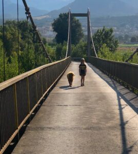 Niña y su mascota paseando por un puente en un idílico paisaje de una region rural de l'Alt Urgell