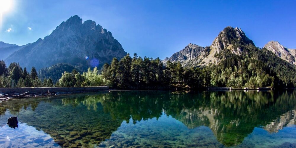 Magnificent view of the Estany de Sant Maurici, its emerald blue-green waters reflecting, as if it were a mirror, the surrounding mountains. Impeccable blue sky.