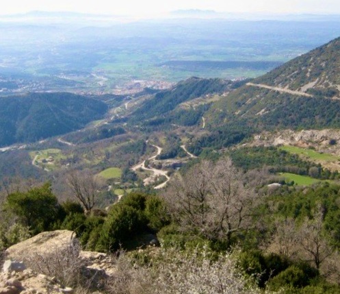 View of the valley from the mountain with its winding roads in the background surrounded by large forests.