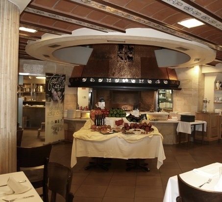 Interior del restaurante La Huerta en su zona central donde se puede ver una chimenea con diversos alimentos expuestos y botellas de vino